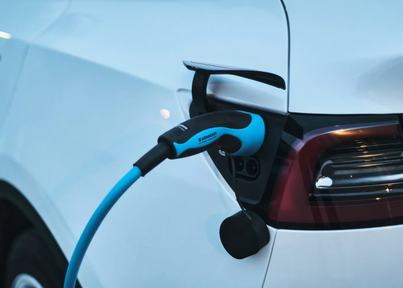 A white electric car plugged into a charger with a blue cable